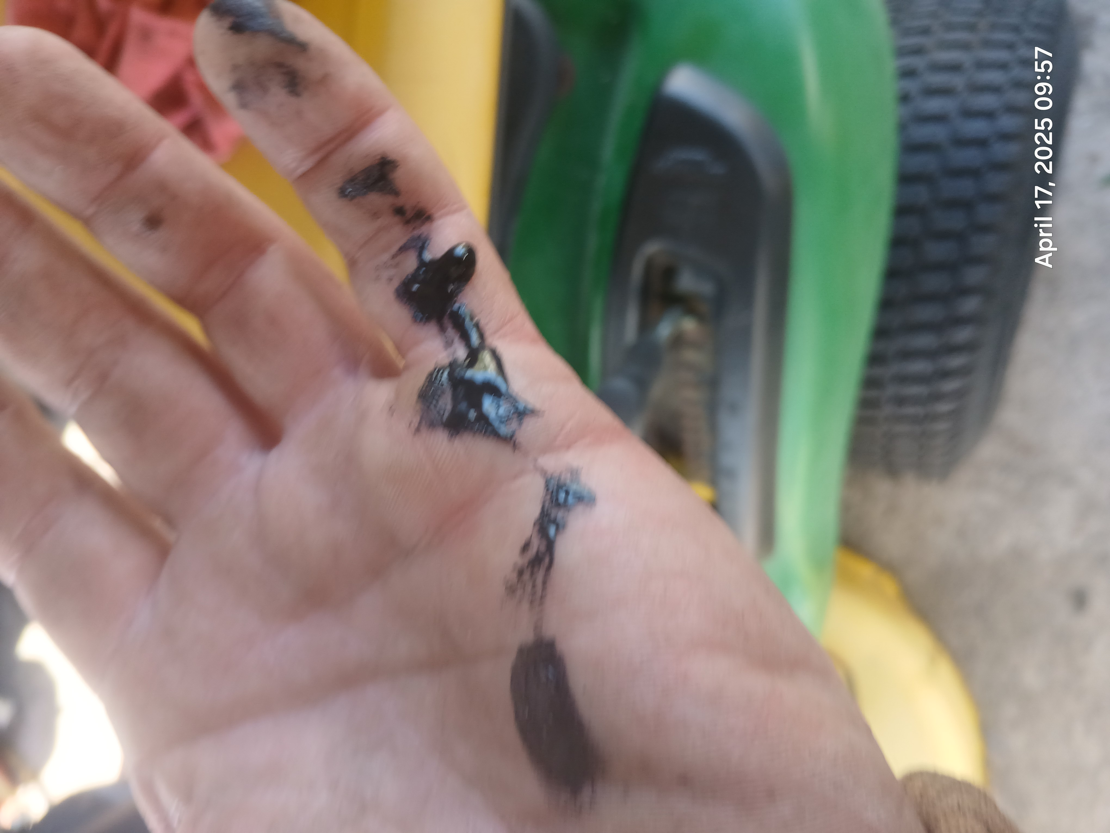Mechanic's hand covered in black liquefied rubber from an ethanol-degraded fuel line removed from a small engine